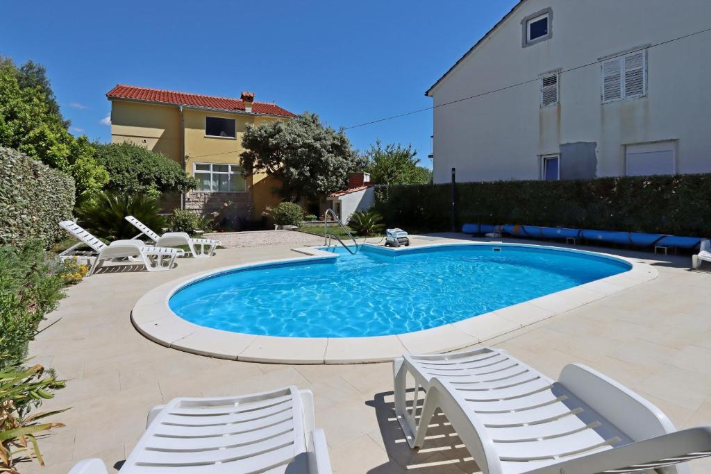 a swimming pool with white chairs around it at Family-friendly apartments with swimming pool Banjol, Rab - 5007 in Rab