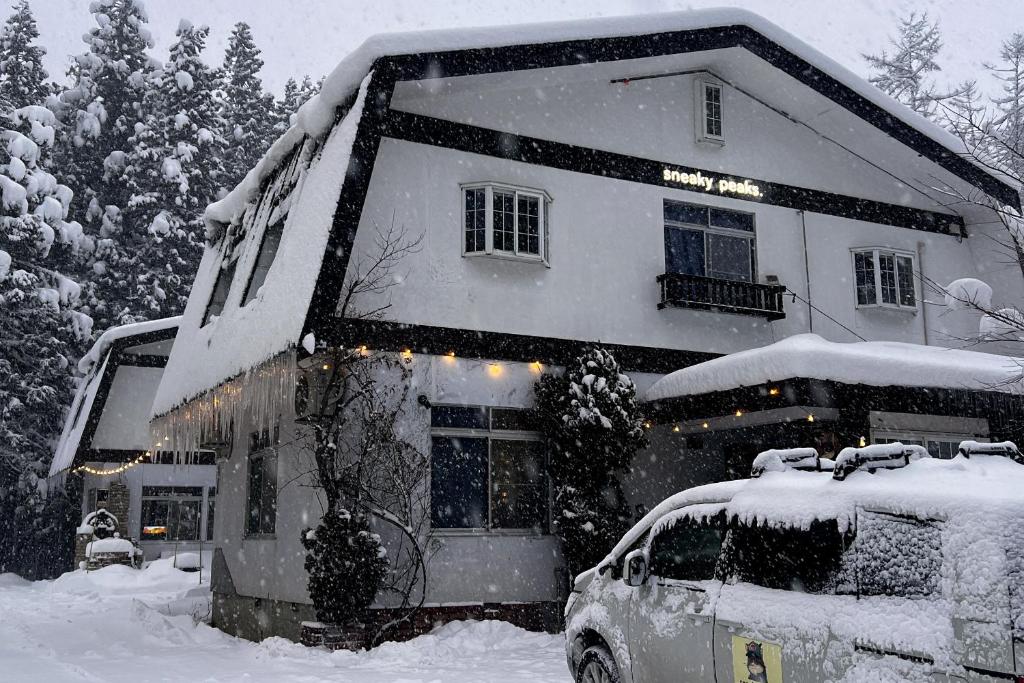 a snow covered house with a car parked in front of it at sneaky peaks in Hakuba