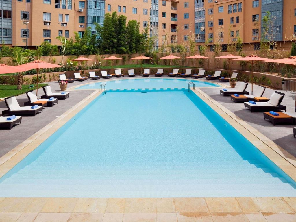 a swimming pool at a hotel with chairs and umbrellas at Novotel Marrakech Hivernage in Marrakesh