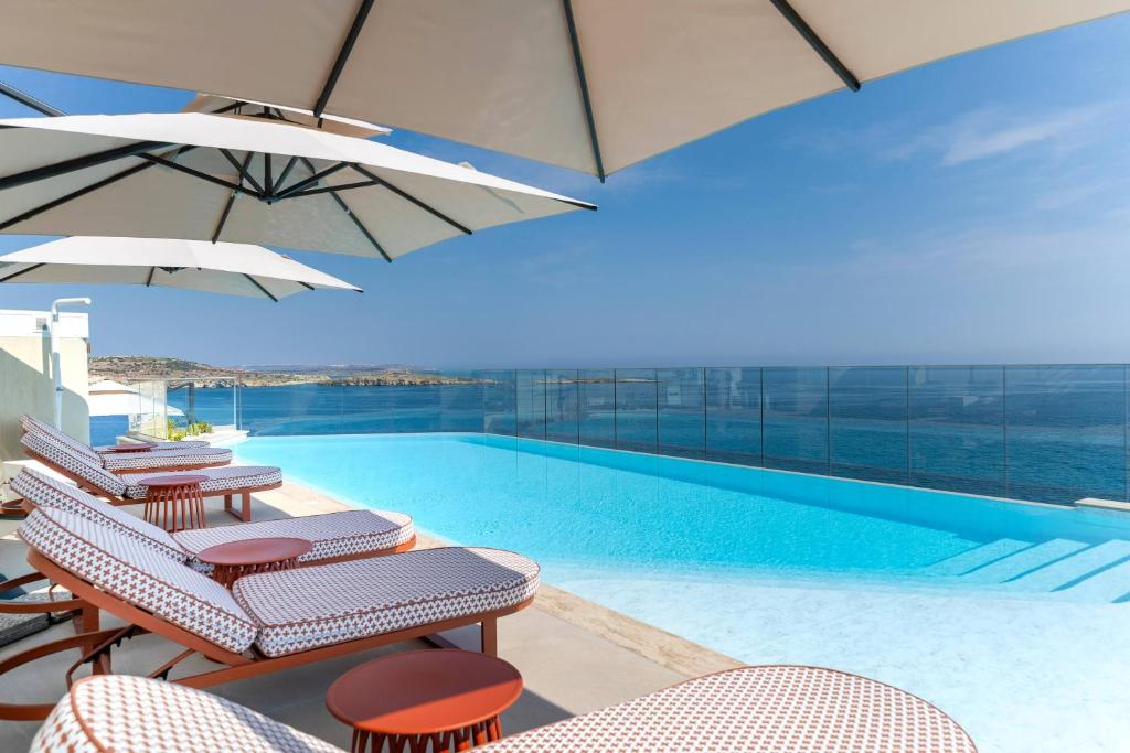 a swimming pool with lounge chairs and umbrellas at INNSiDE by Meliá Bugibba in St. Paul's Bay