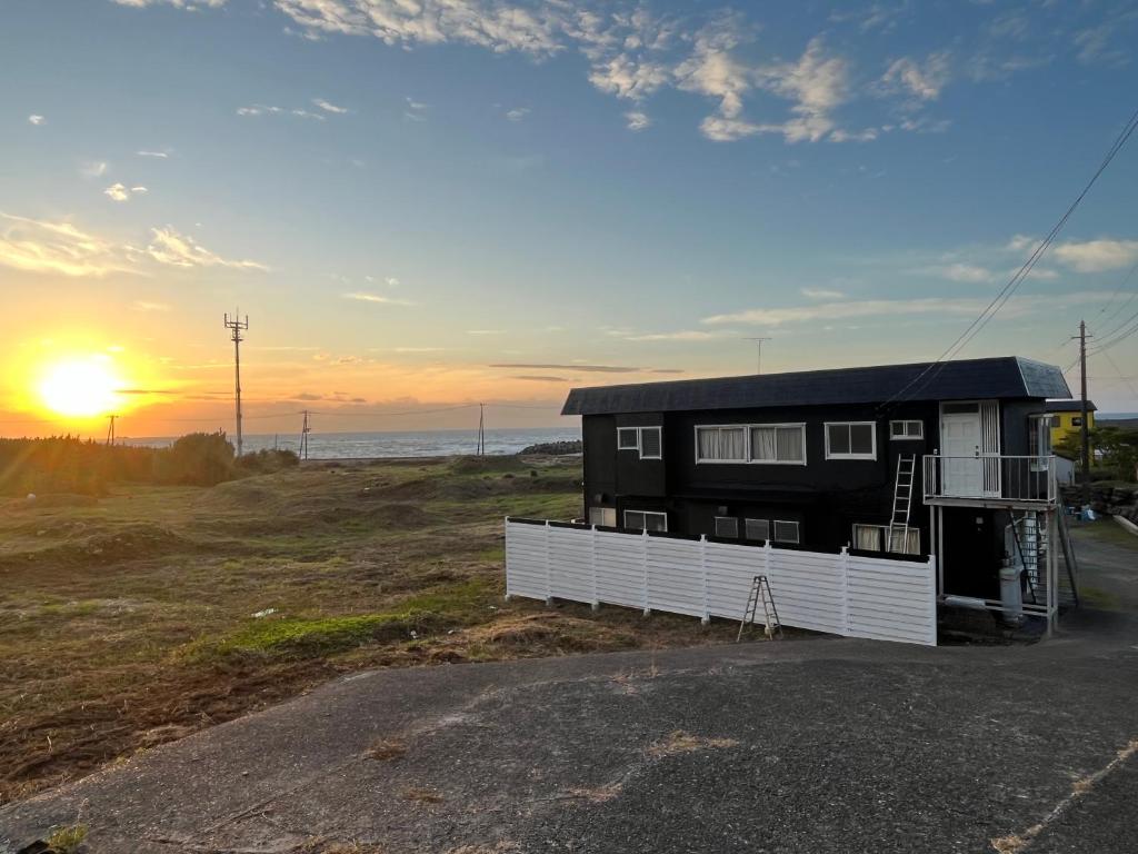 a house on the beach with the sunset in the background at 海岸道路沿い 磯の宿 in Minamiboso