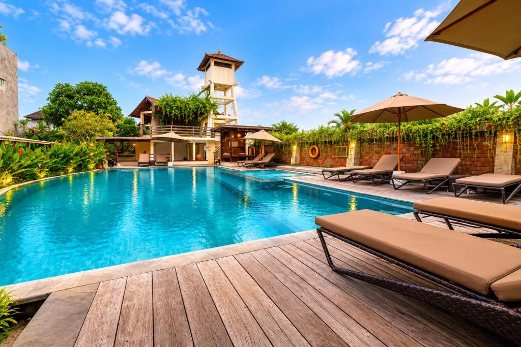a swimming pool with a deck with chairs and umbrellas at Bali Ayu Hotel & Villas 10 Minutes Walking Distance to the Beach in Seminyak