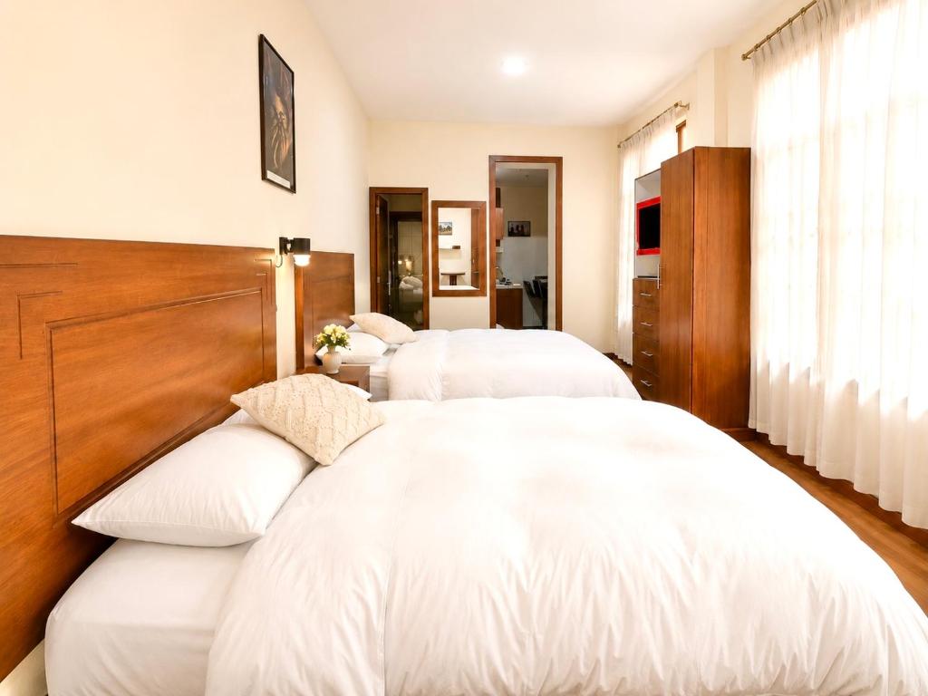 two beds in a hotel room with white sheets at Suite Tarqui en el Centro Histórico in Cuenca