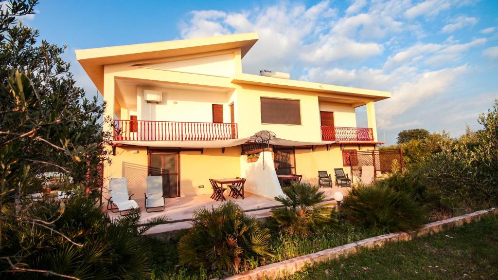 Una gran casa amarilla con sillas y mesa. en Case Bongiovi, en Sciacca