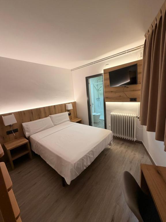 a bedroom with a white bed and a television at El 9 Baral-la in Sant Pau de Segúries