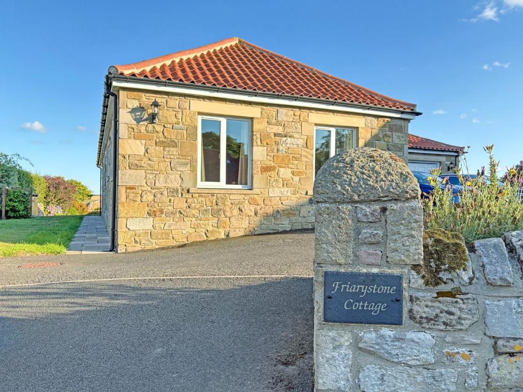 a stone house with a sign in front of it at Friarystone Cottage in Bamburgh