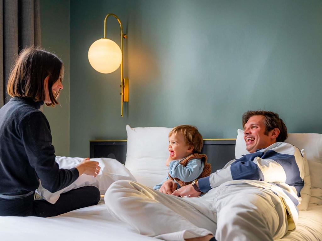 a man and a woman sitting on a bed with a child at Mercure Nantes Centre Passage Pommeraye in Nantes