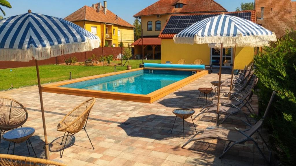 a pool with chairs and umbrellas next to a house at Pearl Home in Békéscsaba