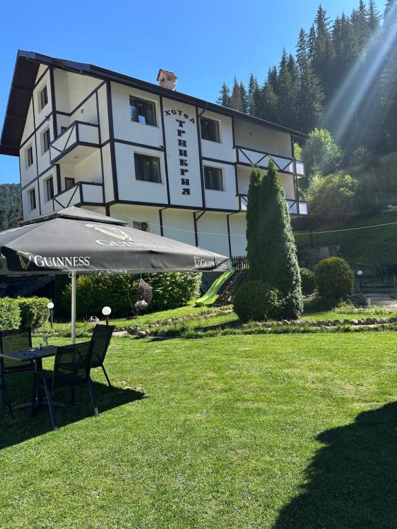 a building with a table and an umbrella in the grass at TRIIBRIA Guest house in Trigrad