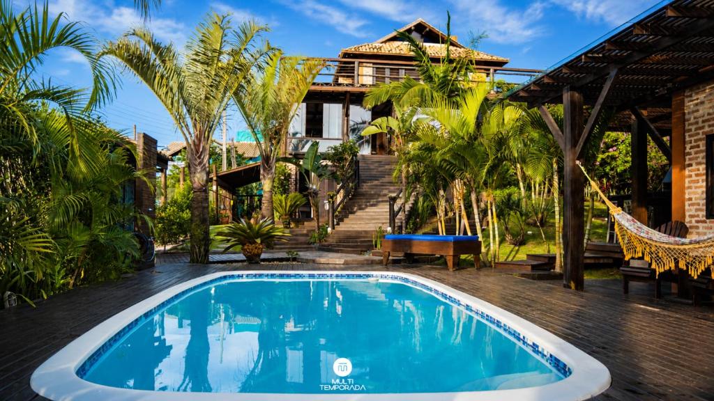 a swimming pool in front of a house with palm trees at Ibiraquera Life in Praia do Rosa