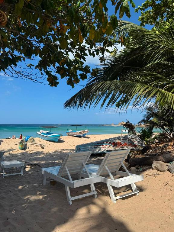 two lounge chairs on a beach with boats in the water at Diving Club Beach Resort in Trincomalee