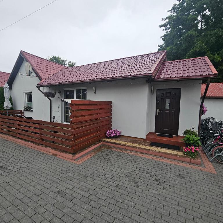 a small white house with a wooden fence at Domki Oliwia in Łeba