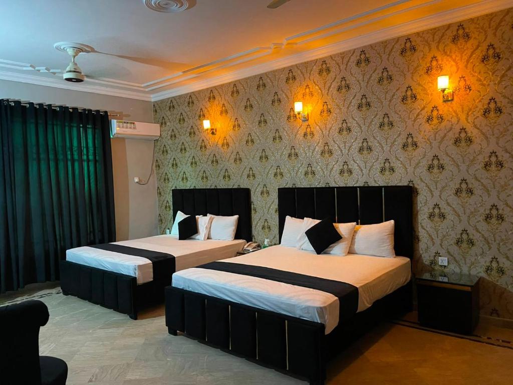 a bedroom with two beds and a wall with wallpaper at Oasis Family Hotel in Lahore