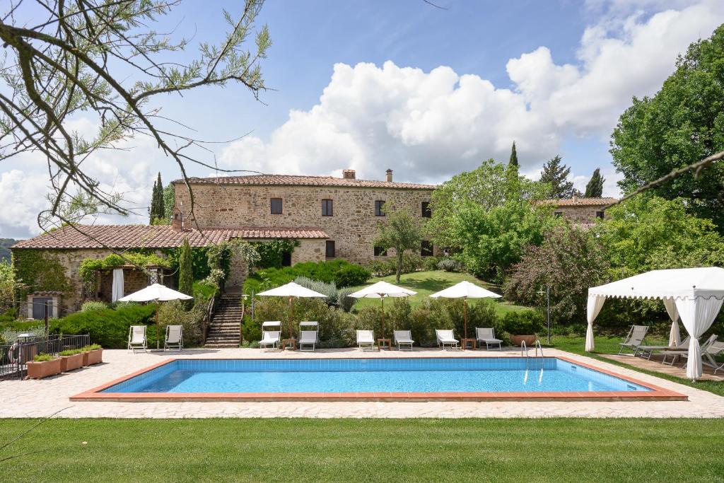 a pool with chairs and umbrellas in front of a building at Agriturismo Piettorri in Casole dʼElsa