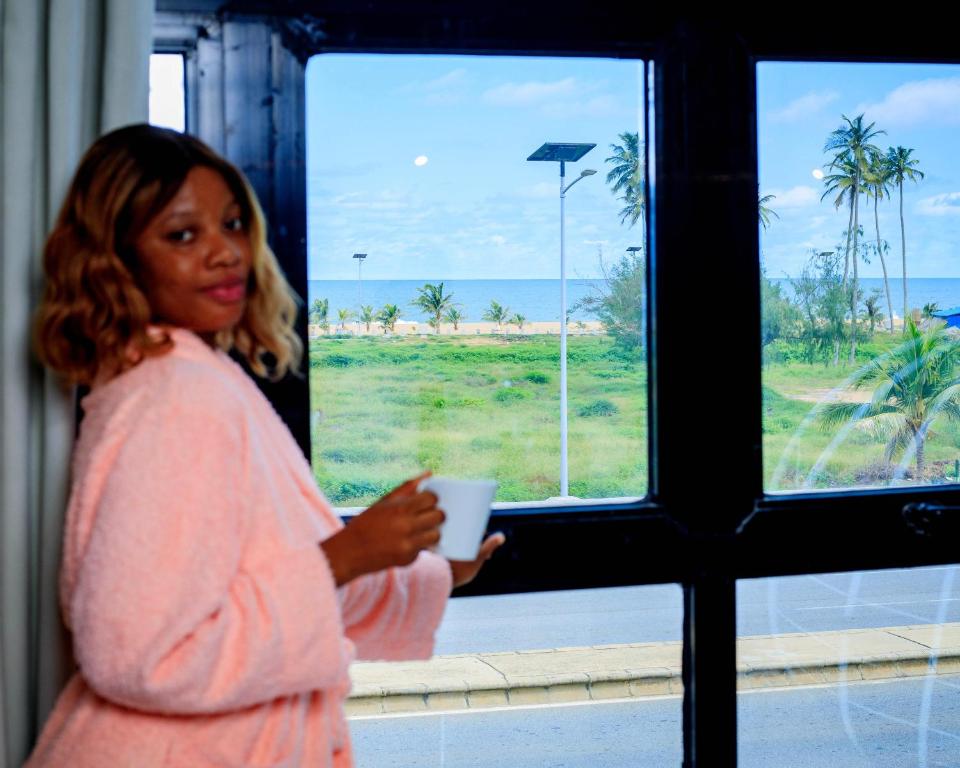 a woman is looking out a window at the beach at CHROME Résidences Fidjrossè PLAGE in Cotonou