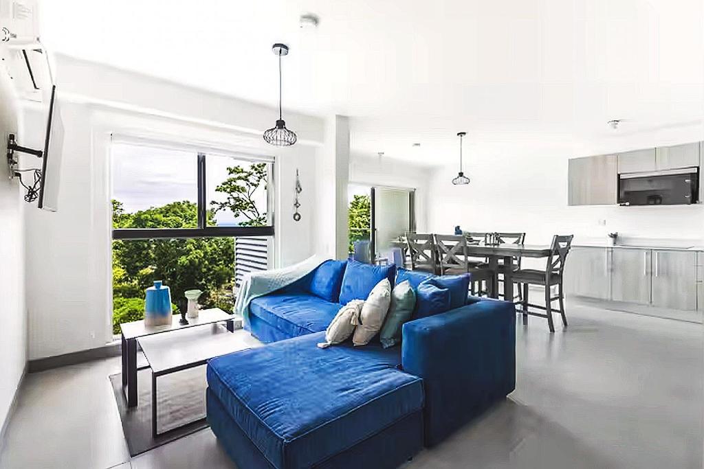 a living room with a blue couch and a kitchen at Playa Mantas - 7th Floor - Sea View - Beach Club Access - Balcony - Beach in Punta Leona