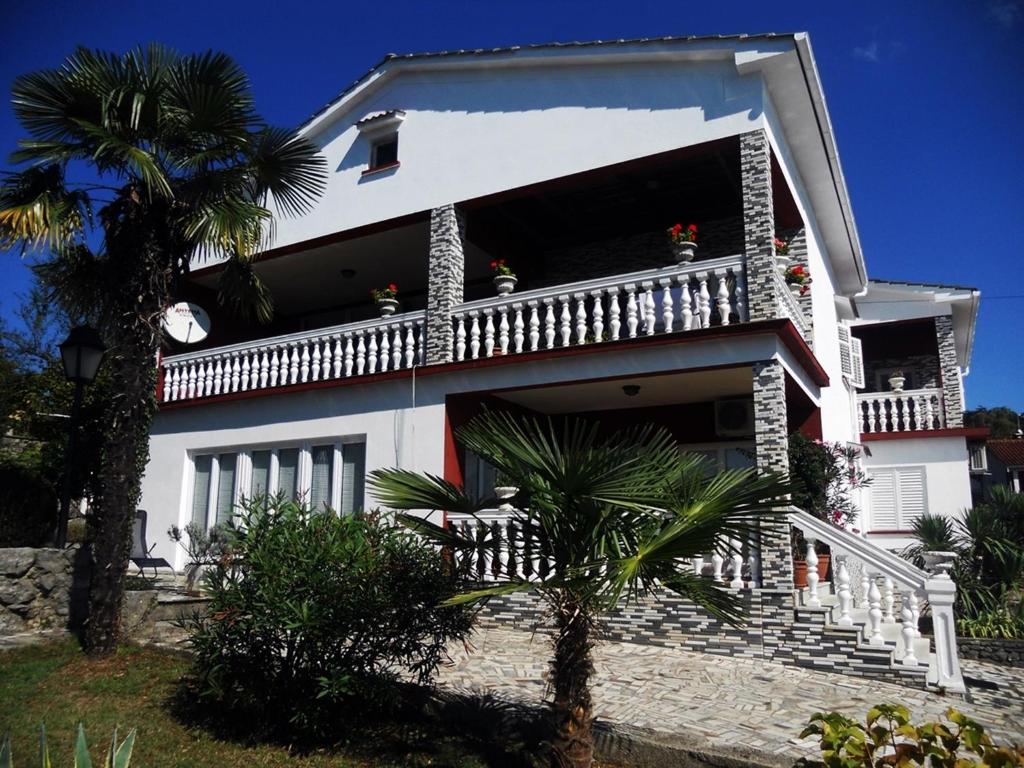 a white house with a balcony and a palm tree at Apartment Milano in Matulji