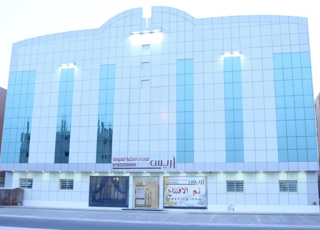 um grande edifício de vidro com uma placa em frente em Aris Furnished Apartments em Buraydah