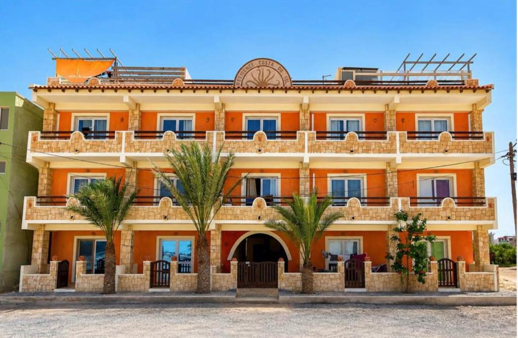 an orange building with palm trees in front of it at Attico Residence Costa do Sol in Sal Rei