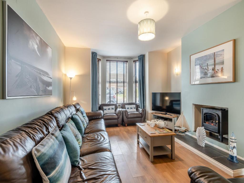 a living room with a leather couch and a fireplace at Samphire in Bacton