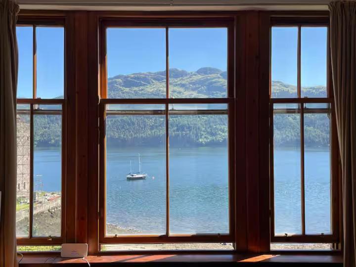 a window with a view of a boat in the water at Stunning Hideaway on Loch Goil in Carrick