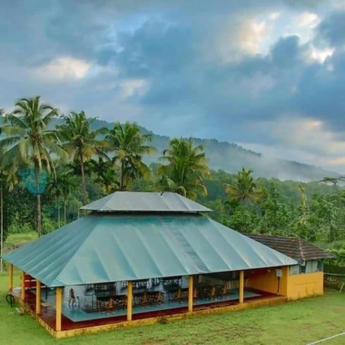 a building with a blue roof and palm trees at Birds Murmur Camp in Kotamangalam