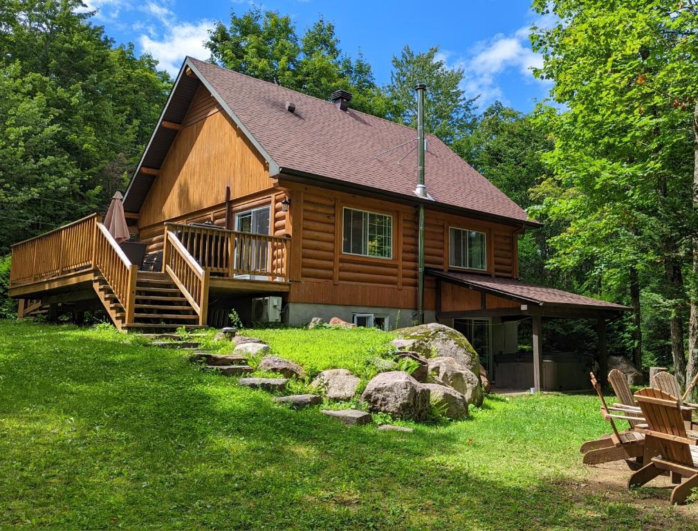a log cabin with a porch and stairs to the front at Chalet Le Boisé SPA et Rivière in Brownsburg