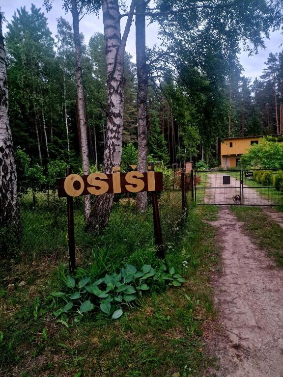 a sign in the grass next to a dirt road at Osīšu Priežu māja in Ķesterciems