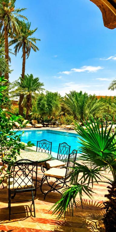 a table and chairs next to a pool with palm trees at Riad Kasbah Le Touareg in Merzouga