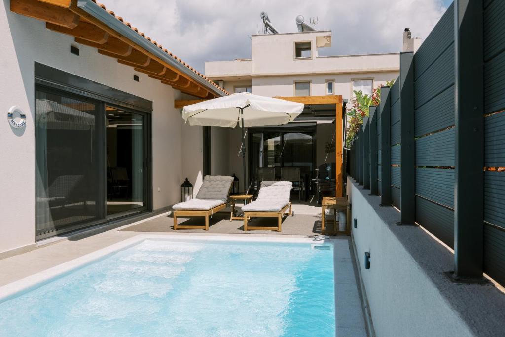 a swimming pool with two chairs and an umbrella at Odysseas Seaside Escape by Philoxenia in Artemida