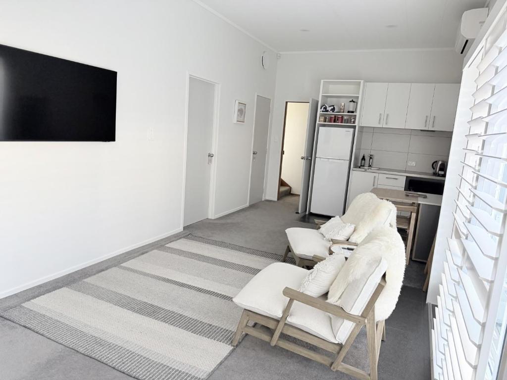a white living room with two chairs and a tv at Ohope Coastal Escape in Ohope Beach