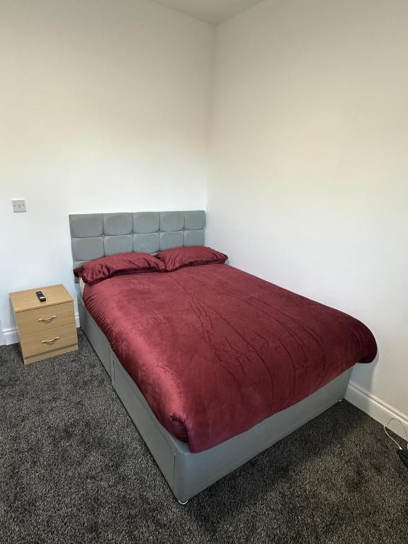 a bedroom with a bed with a red blanket and a night stand at Plus Properties Leeds 2 in Bradford