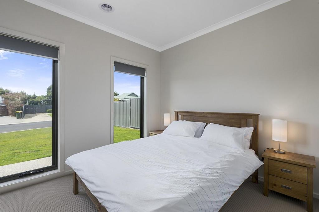a white bedroom with a bed and a large window at SUNRISE ON APOLLO in Apollo Bay