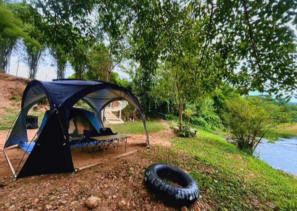 a tent with a tire in front of it next to a lake at สุขเสมอ แคมป์ปิ้ง สวนผึ้ง in Ban Tha Khoei