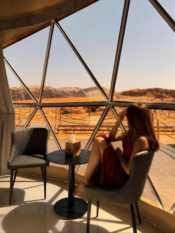 a woman sitting in a chair in front of a window at WADI RUM REGENCY BUBBLE lUXURY in Wadi Rum