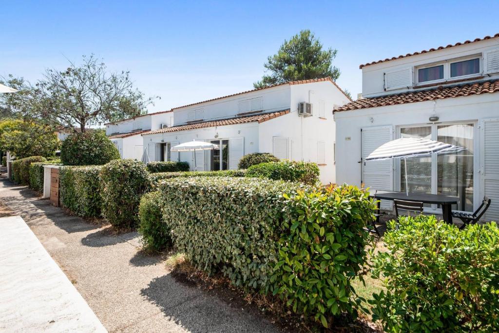 a white house with bushes and an umbrella at Comfort Aparthotel Mandelieu la Napoule Village in Mandelieu-La Napoule
