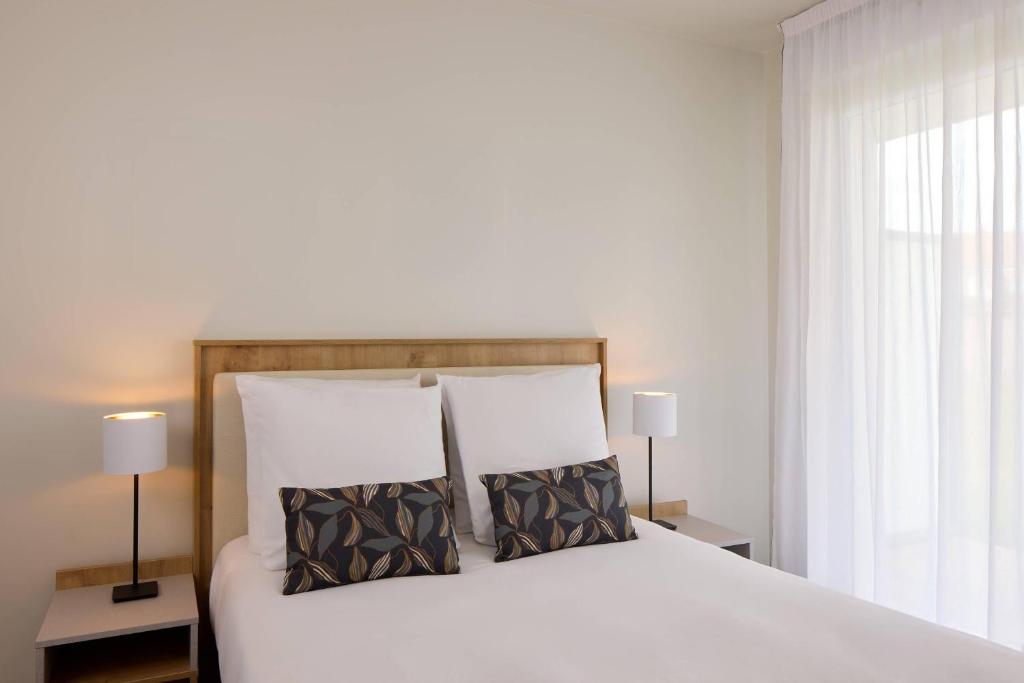 a bedroom with a large white bed with two pillows at Quality Aparthotel Villefontaine in Villefontaine