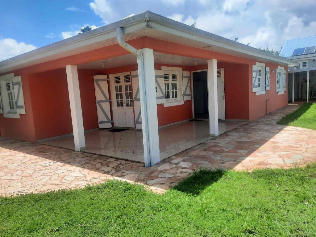 a red house with white columns in a yard at Villa Le Balisier in Le Lamentin