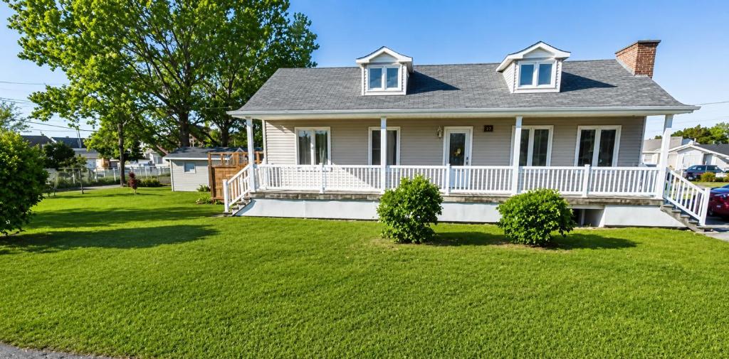 a house with a white porch and a yard at Chez nous ailleurs in Sainte-Anne-des-Monts