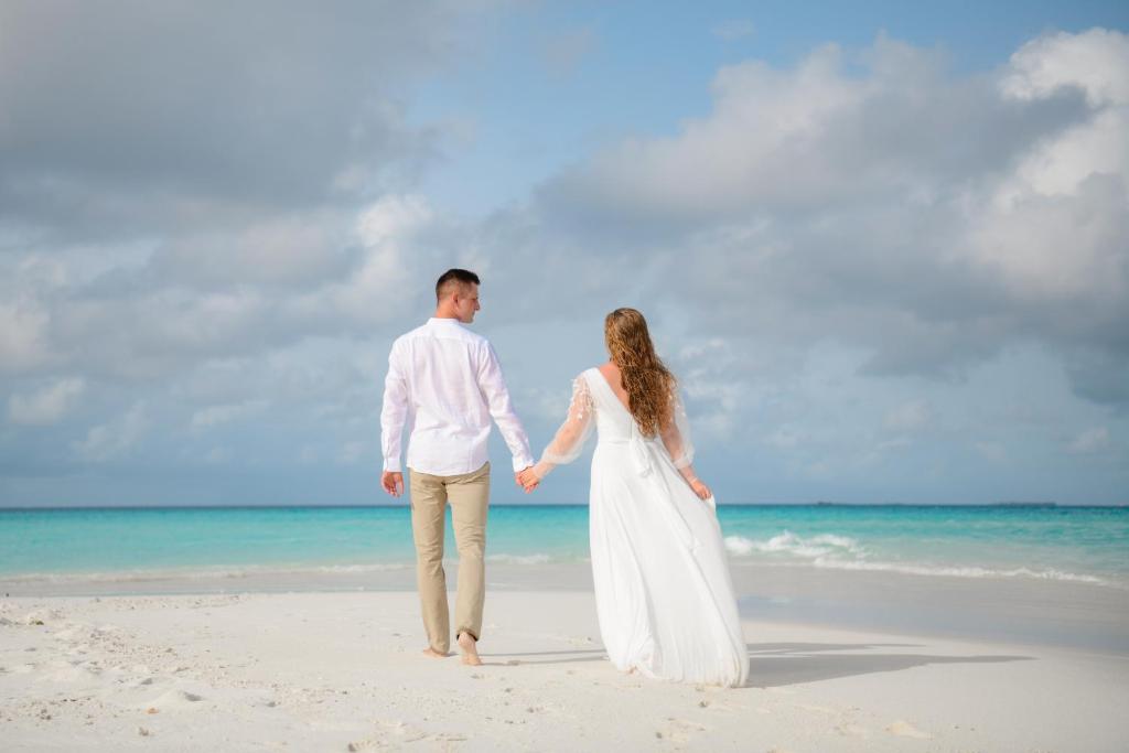 a bride and groom walking on the beach at Fali Guest House in Kudahuvadhoo