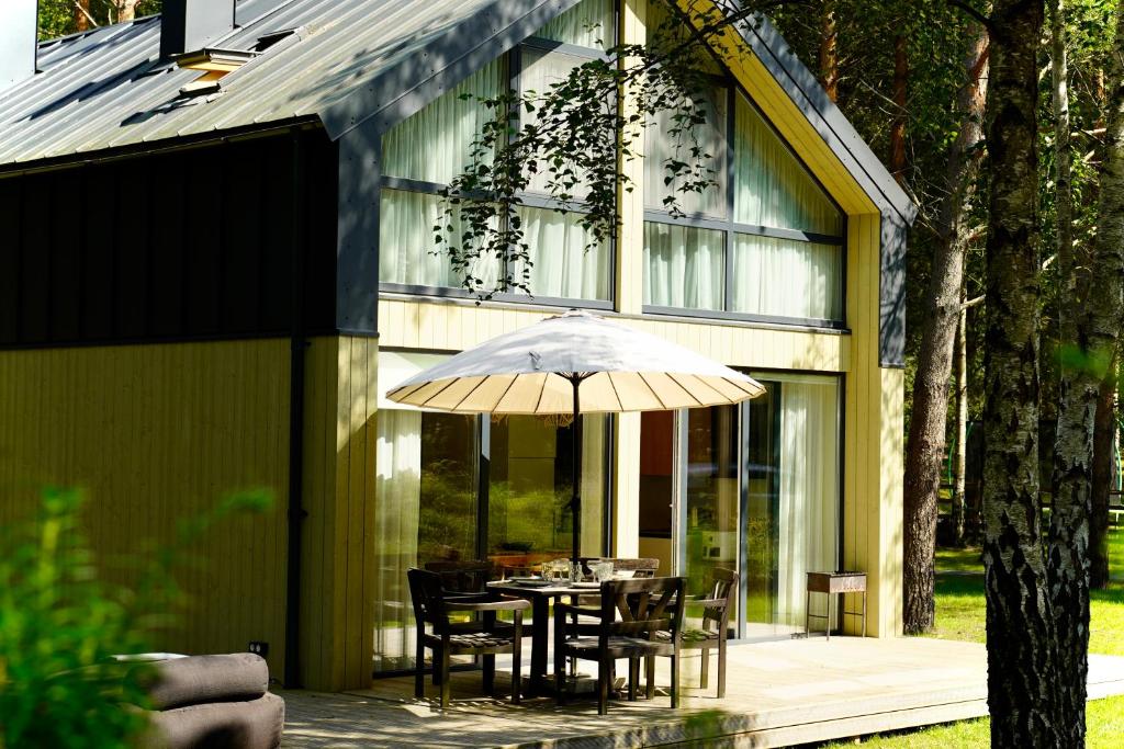 a table with an umbrella in front of a house at Tago Forest - Dune Apartments in Jūrmalciems