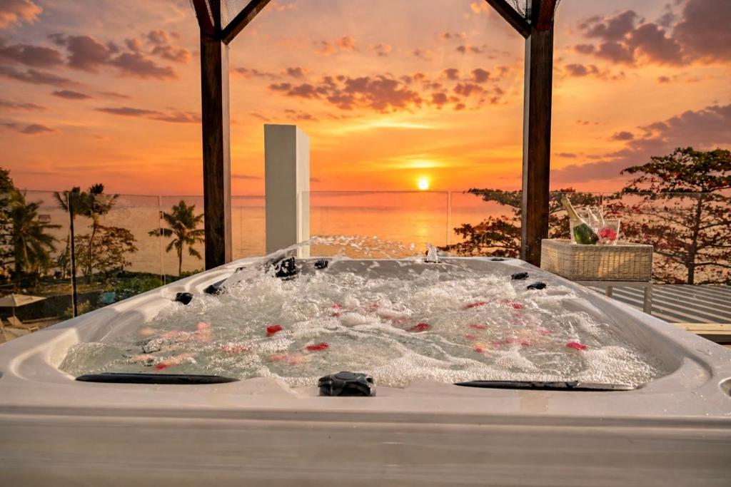a tub filled with water with a sunset in the background at Ocean Point Beachfront Penthouses by Gerards & Angel in Pointe aux Piments