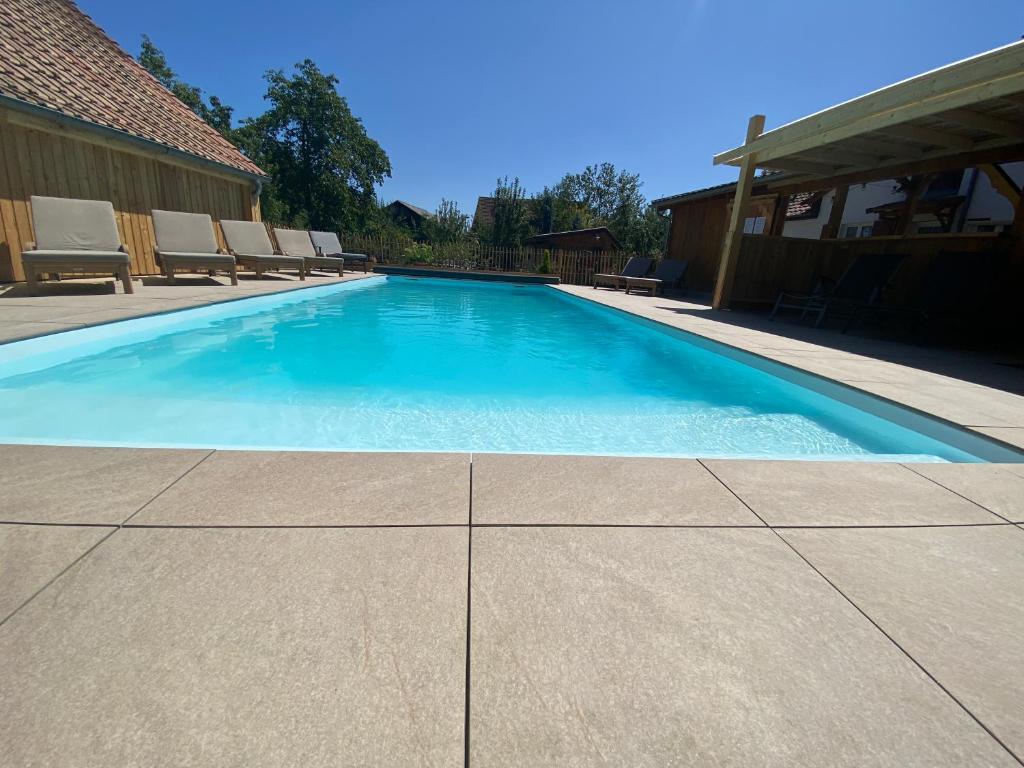 a swimming pool with chairs and blue water at Gîte des roses in Diebolsheim
