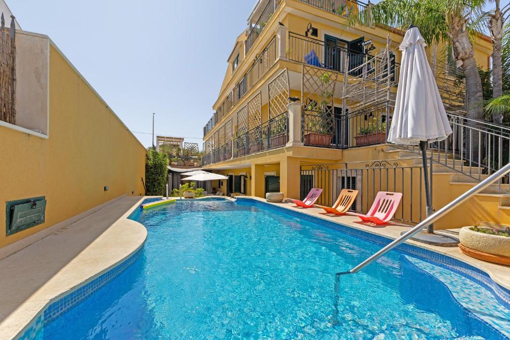 a swimming pool with chairs and an umbrella next to a building at Villa Magda - private pool 20 pax in Marina di Ragusa