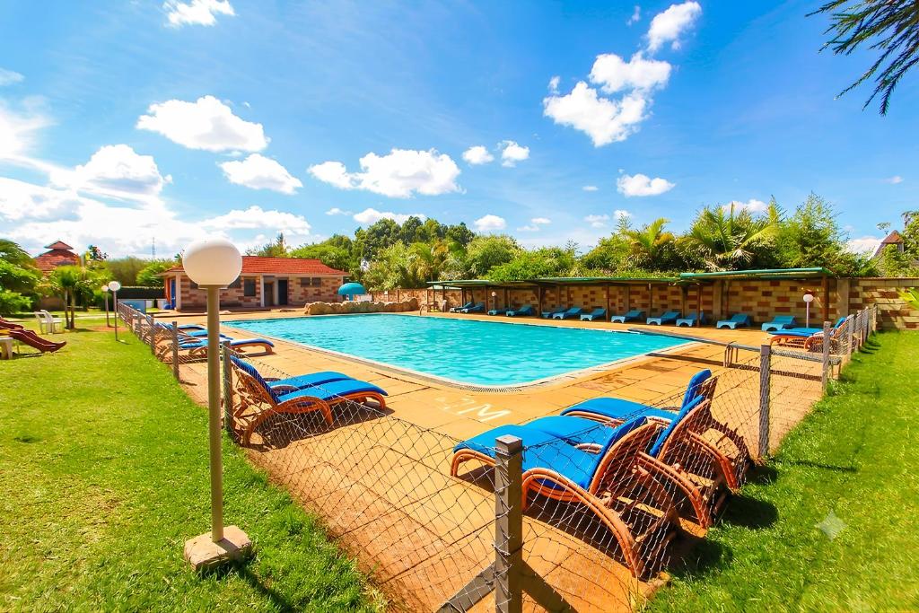a swimming pool with blue chairs in the grass at Poa Place Resort & Hotel - Where Nature Meets Comfort Eldoret in Eldoret