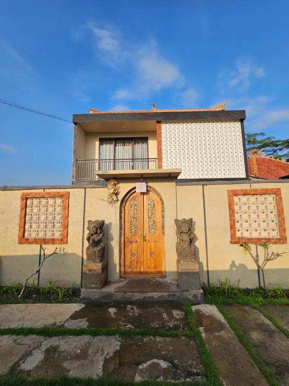 a house with a wooden door and a balcony at Kala Senja Guest House in Sukawati