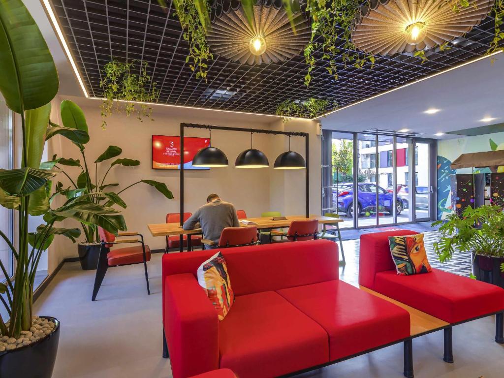 a restaurant with red furniture and a man sitting at a table at ibis Bucharest Politehnica in Bucharest