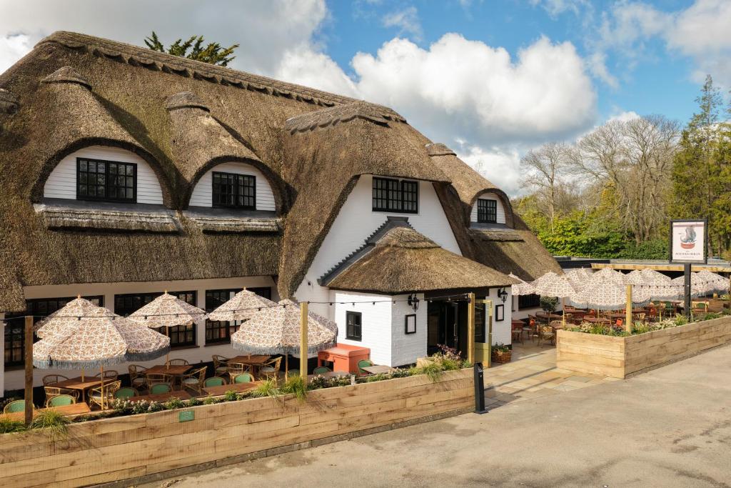 a building with a thatched roof with tables and chairs at The Potters Heron - A Heartwood Inn in Romsey