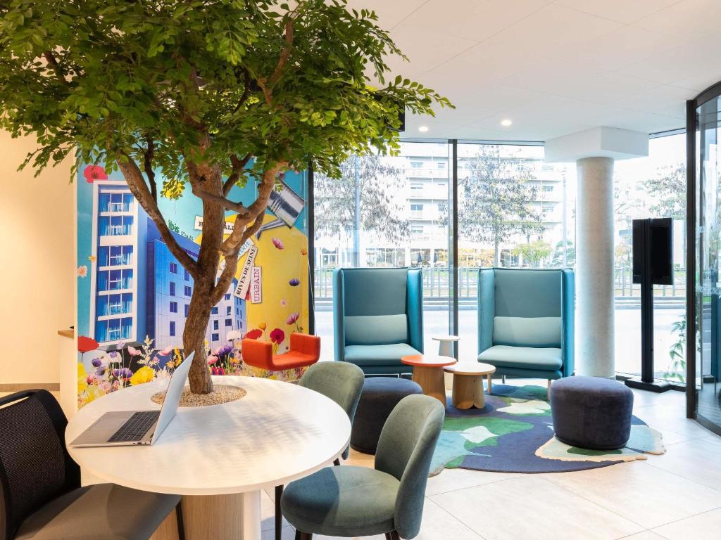 a table and chairs with a tree in a waiting room at ibis Styles Bezons Paris La Défense in Bezons