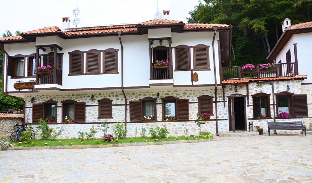 ein weißes Haus mit braunen Fensterläden und einer Bank in der Unterkunft Family Hotel Dinchova kushta in Rozhen